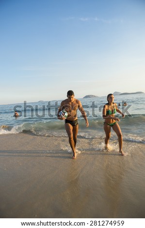 RIO DE JANEIRO, BRAZIL - APRIL 1, 2014: Young Brazilian man and woman walk with football on the shore of Ipanema Beach at Posto 9, a famous gathering place for sport and recreation.