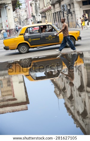 HAVANA, CUBA - JUNE, 2011: Vintage Russian Lada taxi car reflects next to passing pedestrian in a puddle on a street in Central Havana.
