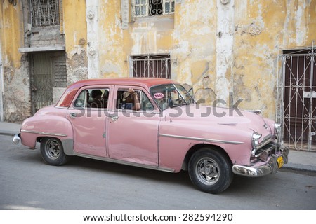 HAVANA, CUBA - MAY, 2011: Vintage American car in pink carries a load of passengers along a weathered street in Central Havana.