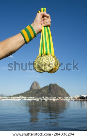 Hand of first place athlete with Brazil colors wristband holding gold medals at Botafogo Beach Rio de Janeiro Brazil skyline
