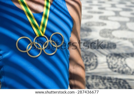 RIO DE JANEIRO, BRAZIL - FEBRUARY 23, 2015: Athlete wearing Olympic rings gold medal standing under palm frond shadows in front of the sidewalk pattern of Ipanema Beach.