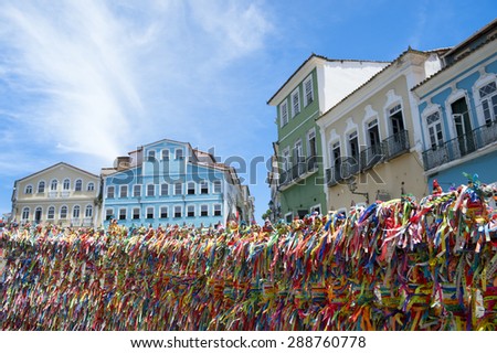 Decorative Brazilian wish ribbons tied to a church gate frame a view of bright colonial architecture of Pelourinho Salvador Bahia Brazil