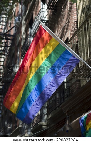 Gay pride rainbow flag flies in the sun against shadows on an old-fashioned fire escape
