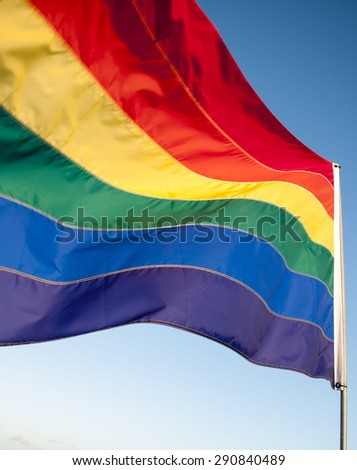 Gay pride rainbow flag waving in bright sunlight against clear blue sky