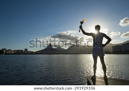 Silhouette of an athlete standing with sport torch against the the setting sun of the Rio de Janeiro Brazil skyline at Lagoa lagoon