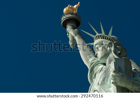 Profile view of the Statue of Liberty holding her torch against clear bright blue sky