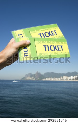 Hand holding pair of Brazil tickets in front of sea view Ipanema Beach in Rio de Janeiro