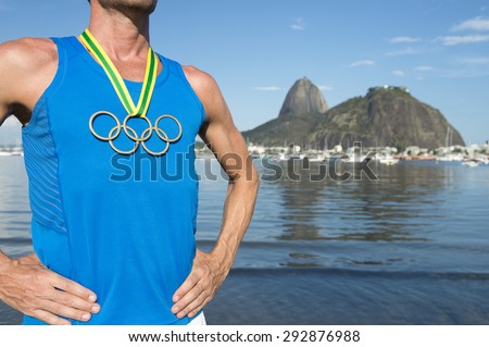 RIO DE JANEIRO, BRAZIL - MARCH 05, 2015: Athlete wearing Olympic rings gold medal in front of city skyline view of Sugarloaf Mountain at Botafogo Bay.