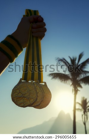 First place athlete holding gold medals in front of the sunset on Ipanema Beach Rio de Janeiro Brazil