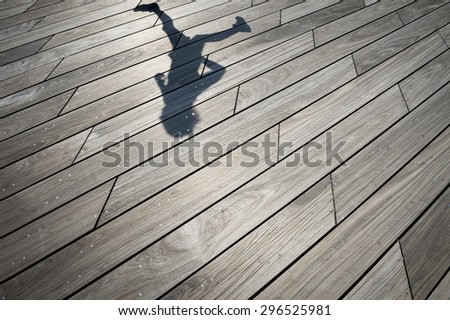 Shadow of runner jogging across weathered smooth wood plank boardwalk background textured with modern angular lines