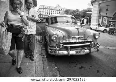 HAVANA, CUBA - CIRCA JUNE, 2011: Cuban pedestrians pass a vintage American car on a street in Centro.