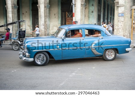 HAVANA, CUBA - CIRCA JUNE, 2011: Cubans drive in old American car in front of typical local architecture.