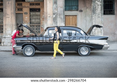 HAVANA, CUBA - CIRCA MAY, 2011: Cuban woman walks by people a classic American car under repair on a street in Old Havana.