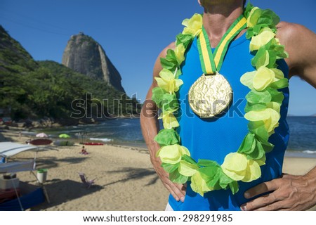 First place athlete wearing gold medal and Brazil colors lei standing outdoors in front of Sugarloaf Mountain Rio de Janeiro