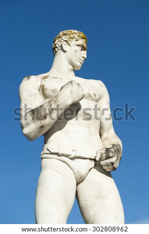 Ancient marble statue of muscular boxer against bright blue sky