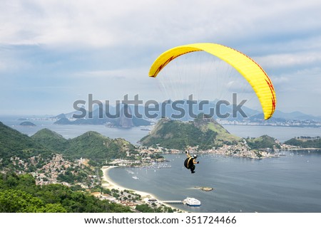 Bright yellow hang glider flying over the mountainous skyline of the city skyline from a hillside park in Niteroi, Rio de Janeiro, Brazil