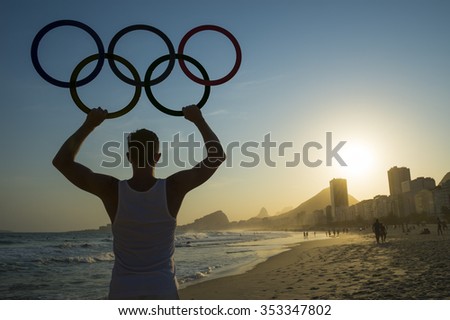 RIO DE JANEIRO, BRAZIL - OCTOBER 30, 2015: Athlete holds Olympic rings above sunset city skyline view of Copacabana Beach at Leme.