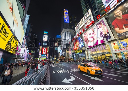 NEW YORK CITY, USA - DECEMBER 22, 2015: Yellow New York taxi passes crowds gathering under the bright lights of Times Square in the build-up to New Year\'s Eve.