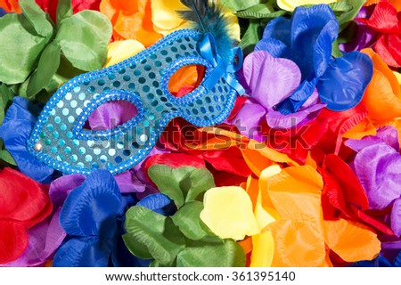 Sparkly blue carnival mask sits on bright background of rainbow colored flower leis in a celebratory pile