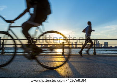 Silhouettes of jogger running and bicyclist cycling at sunset in front of the city skyline