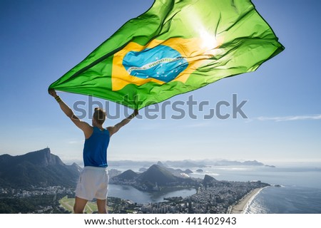 Athlete stands holding a Brazilian flag at a bright overlook of the city skyline of Rio de Janeiro, Brazil