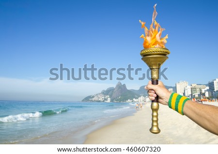 Hand of torchbearer athlete wearing Brazil colors sweatband holding sport torch on Ipanema Beach with Two Brothers Mountain on the skyline of Rio de Janeiro, Brazil