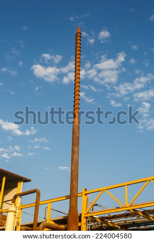 High rusty pipe with a spiral at the chemical plant on a background of blue sky
