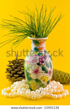 Pines branch in vase with cones and pearl necklace isolated on yellow background