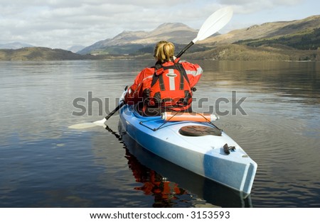 Female kayaker paddling away from the viewer on Loch Lomond with Ben Lomond mountain in the background