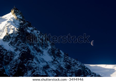 View of Aiguille Du Midi from Chamonix at night with moon in background - landscape orientation