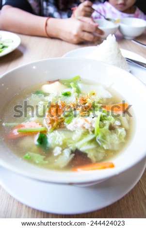 Traditional pork soup with vegetables served in a bowl over table background in Thai restaurant