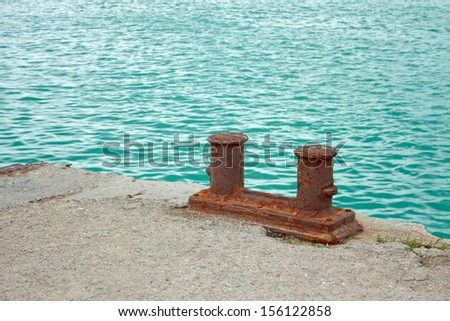 Steel rusty dual mooring bitt on a fragment of old concrete pier on the background turquoise sea water