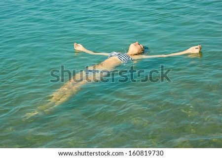 Teen girl lying on the turquoise sea water surface in shallow coastal area