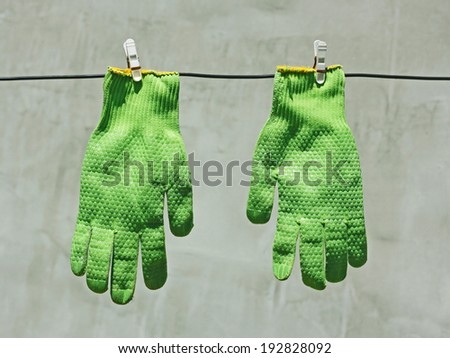 Two vividly green gloves hanging on a wire on a background of gray wall in bright sunlight
