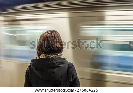 Woman Waiting at a Subway Station with a Train in Motion Pulling into the Platform