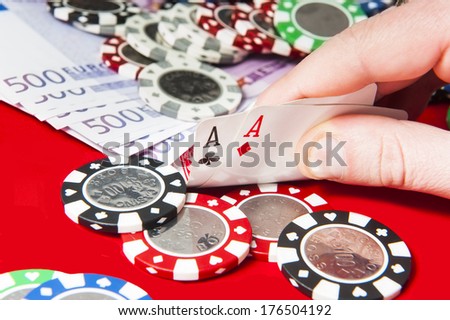Man holding pair of aces poker hand in front of poker chips stack and euro bills