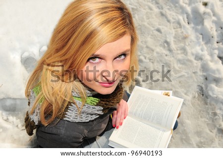 Portrait of pretty blonde girl reading book in winter park