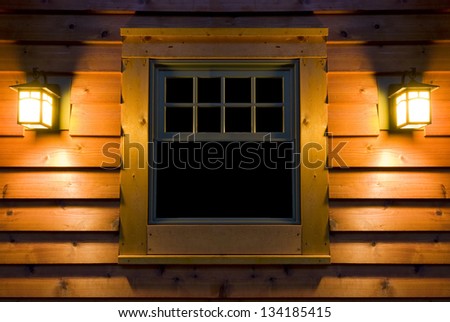 Outside view of cedar cabin window at night with lights on