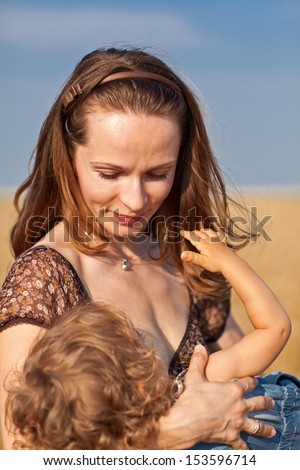 Young woman nurses child against field and sky