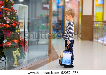 Little boy chooses gifts for the New Year on the background of shop windows