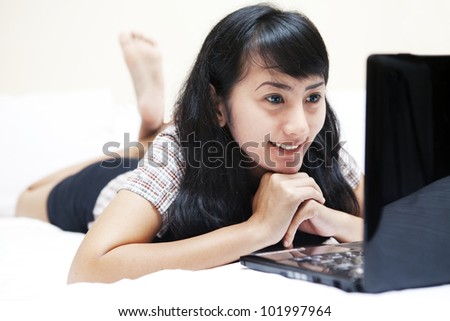 Pretty Asian woman browsing the internet using laptop computer in a bedroom