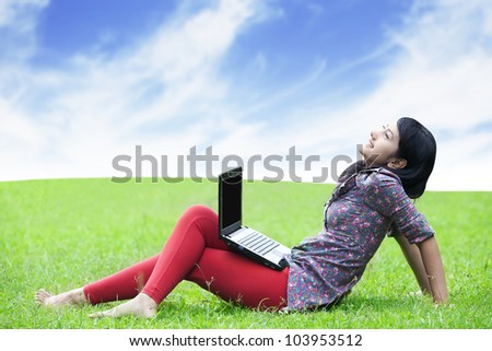Young asian woman with laptop sitting on green grass