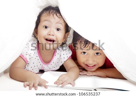 Cute asian siblings reading book under blanket. shot in studio