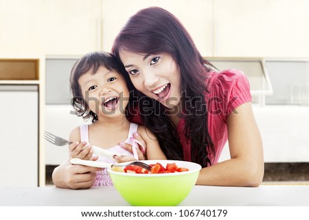 Smiling young asian mother and her daughter with fruit salad. shot in the kitchen