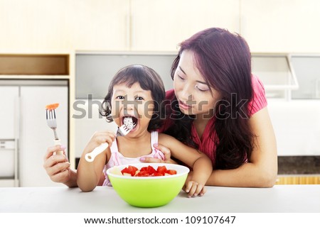Asian young mother helping her daughter eats fresh fruit salad. shot in the kitchen
