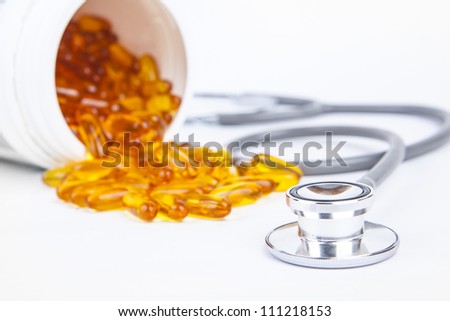 Capsules of fish oil spilled out open container with stethoscope. Shot in studio isolated on white