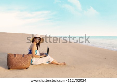 Beautiful asian woman with a bag working on laptop computer at beach