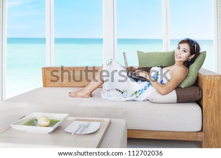 Portrait of beautiful asian woman lying on the couch with laptop and ocean view on the window