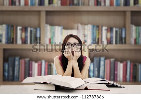 Portrait of frightened female college student with textbooks biting her nails. shot in the library
