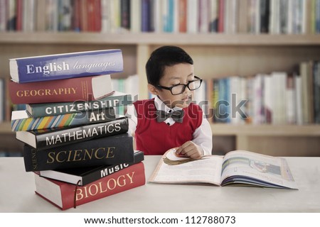 Portrait of little asian elementary school student studying by reading books of lessons. shot in the library